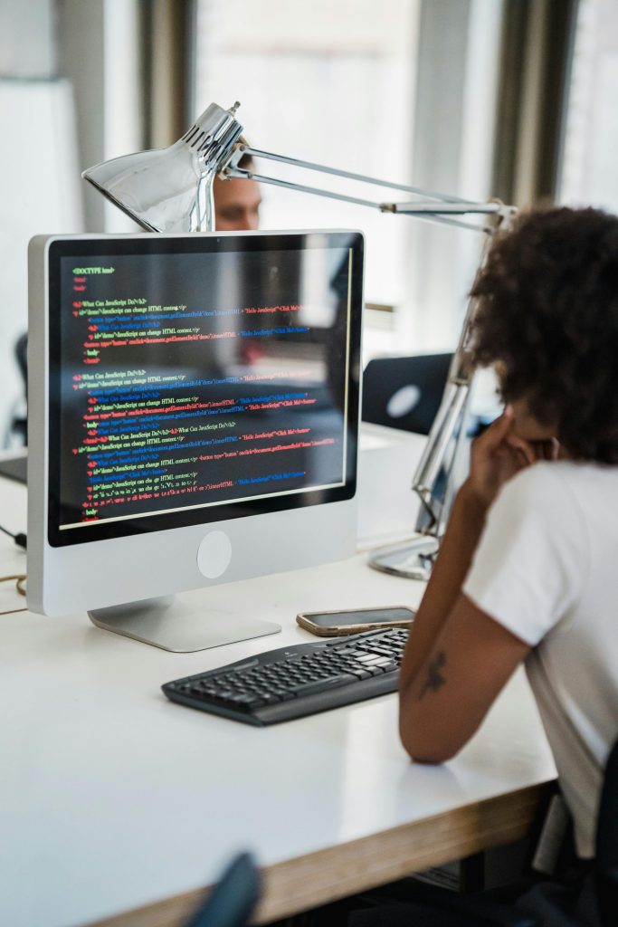 A female professional focused on coding at her office desk with a desktop computer.
